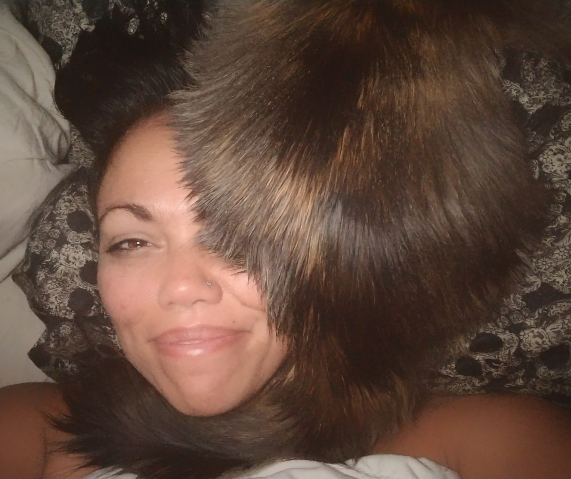 Malia lying on a pillow, smiling, with Teja curled around her head and neck